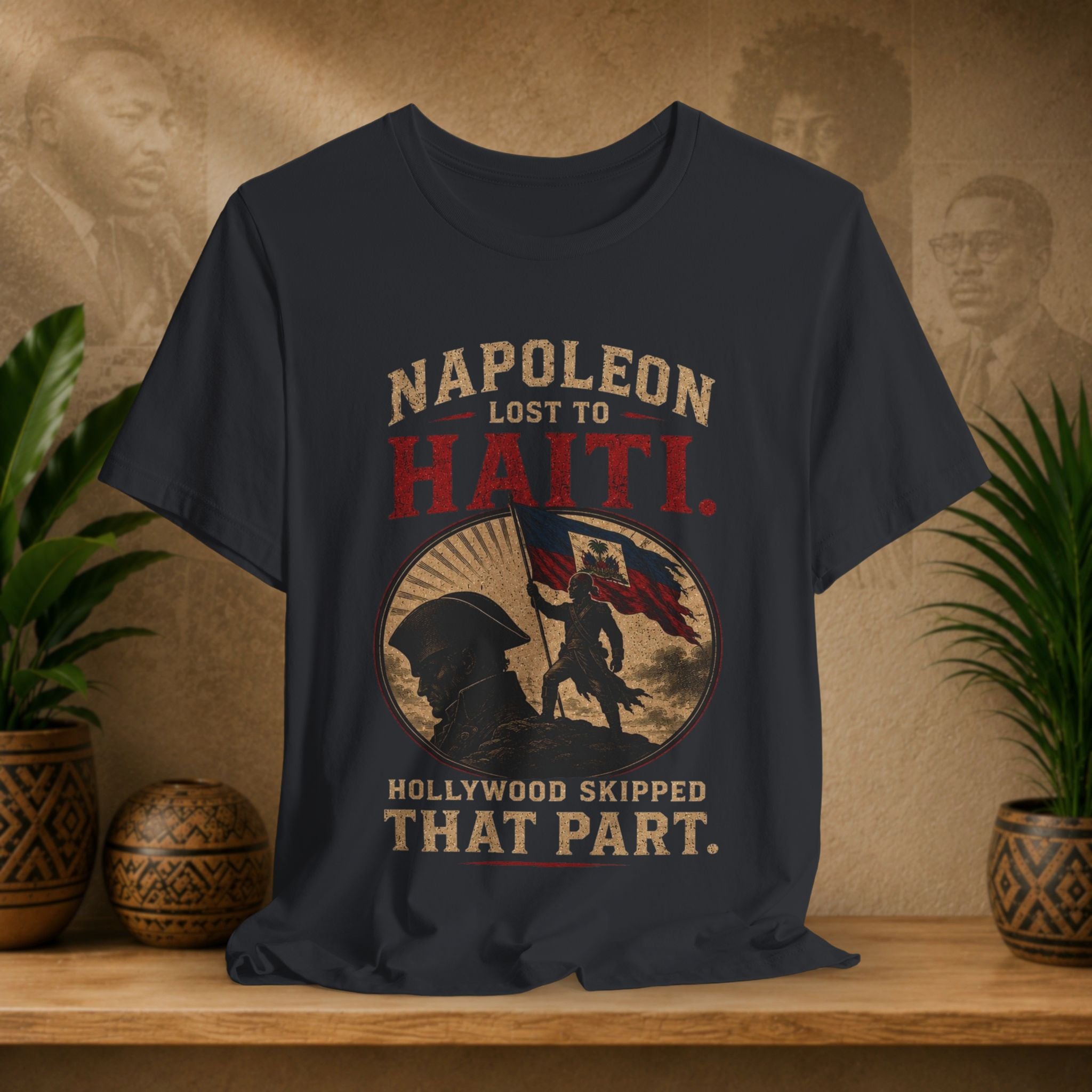 Napoleon Lost to Haiti t-shirt on a wooden surface with decorative plants and background.