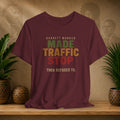 A maroon short-sleeve graphic T-shirt displayed on a wooden surface, with a printed slogan reading 'Garrett Morgan Made Traffic Stop Then Refused To.' in green, tan, and red lettering.