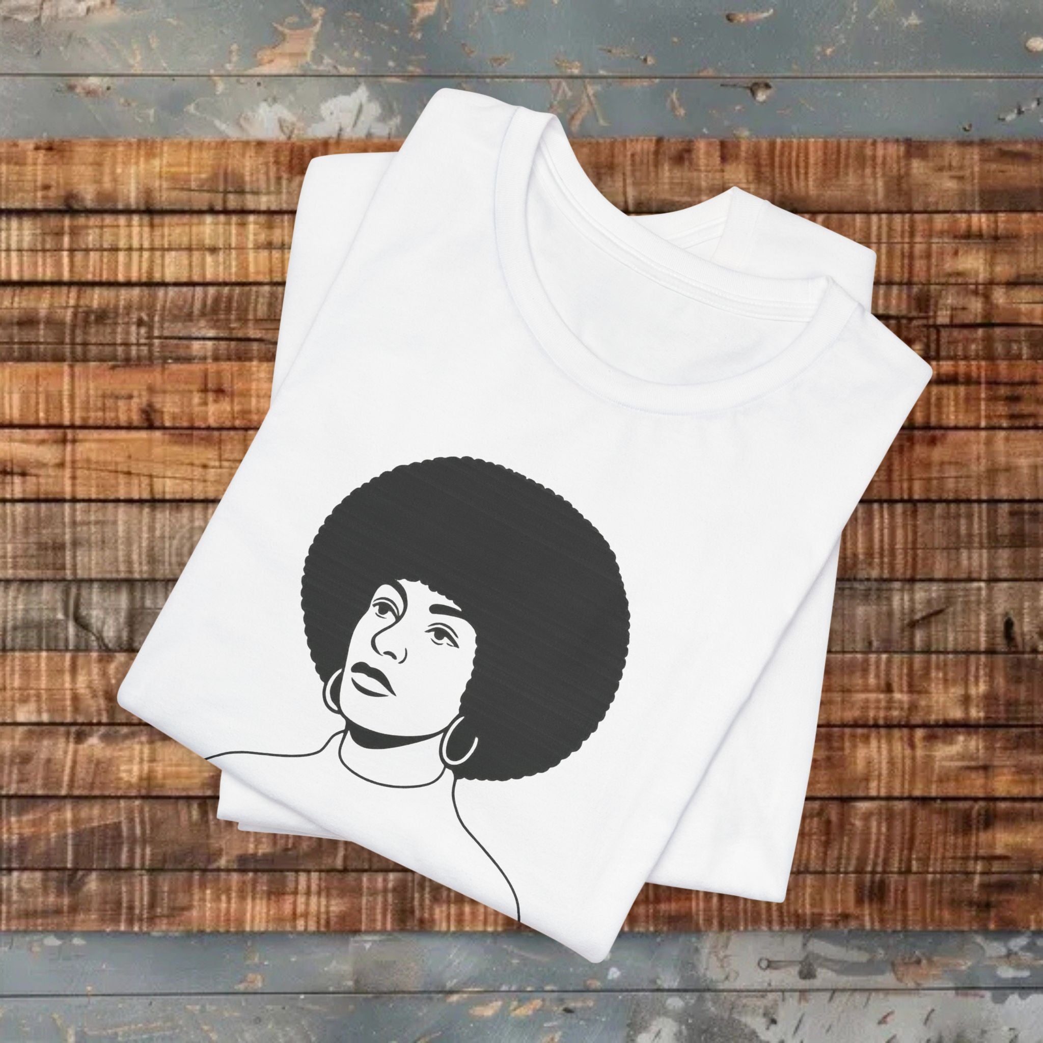 White t-shirt with a black and white graphic of a woman with an afro on a wooden surface