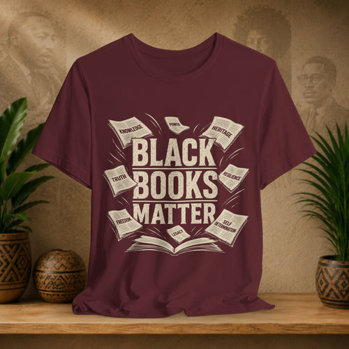 Maroon t-shirt with 'Black Books Matter' design on a wooden surface with plants and a textured wall in the background.