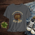 Gray t-shirt with 'Easily Distracted by Hip Hop' graphic on a wooden surface with jeans and sneakers.