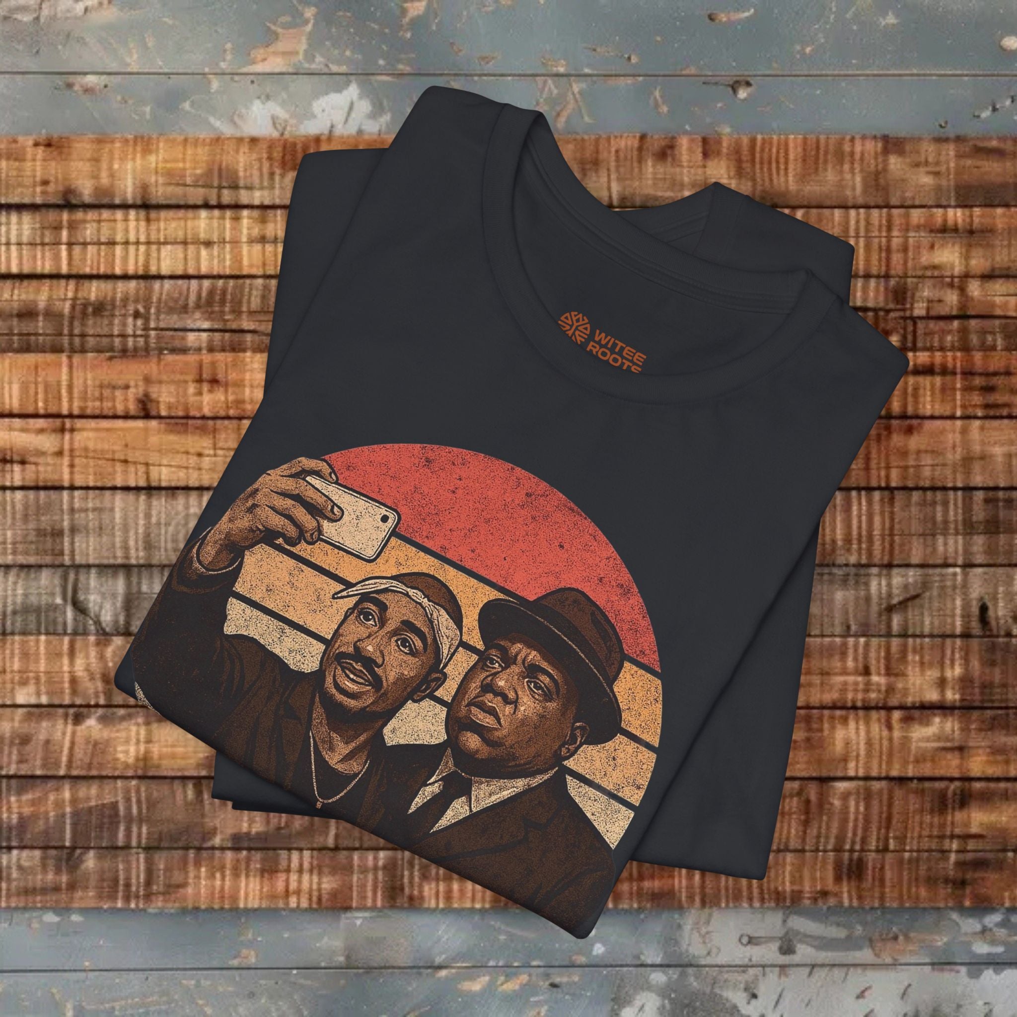 Folded black t-shirt with a graphic of two men taking a selfie on a wooden surface