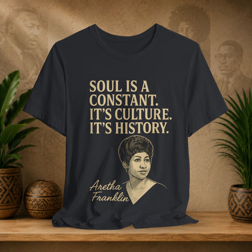 Black t-shirt with Aretha Franklin graphic and quote on a wooden surface with plants and wall art in the background