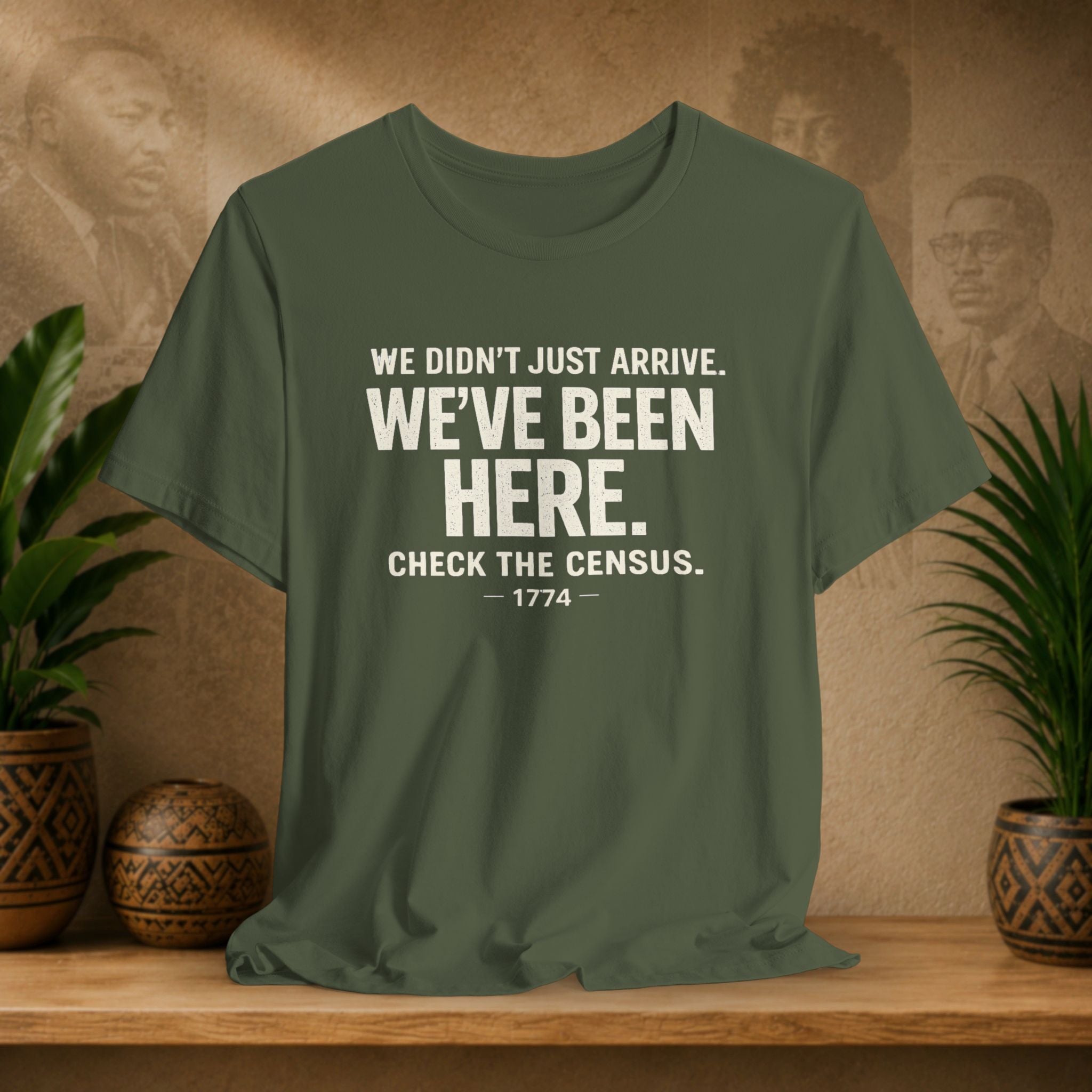 Green t-shirt with white text on a wooden surface with plants and a textured wall background