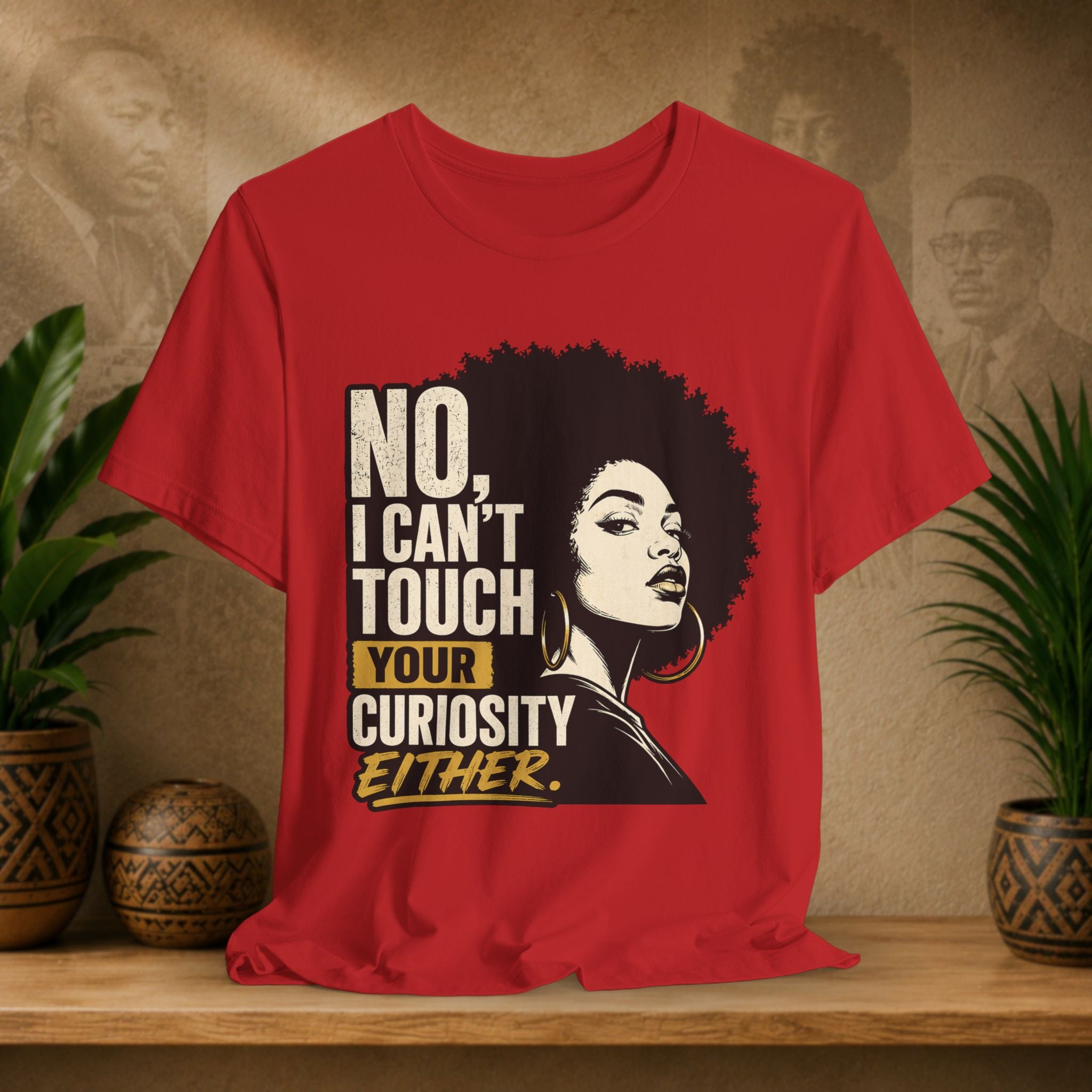 Red t-shirt with a graphic of a woman's face and text on a wooden surface with plants and a textured wall in the background.