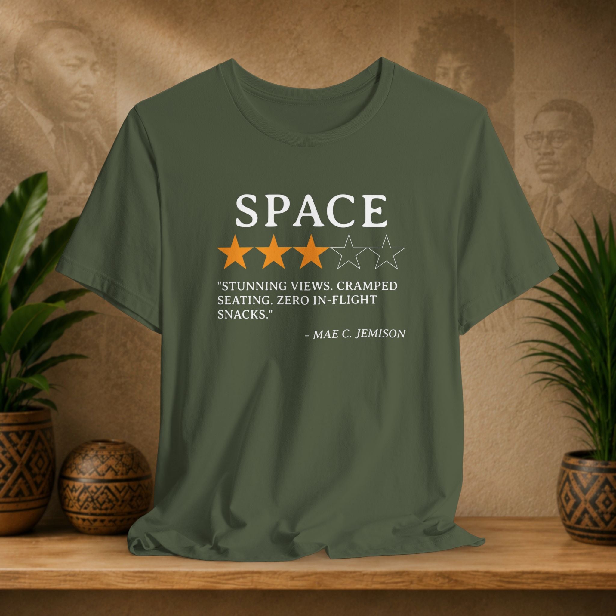 Green t-shirt with space-themed graphic and text on a wooden surface with plants and a decorative wall.