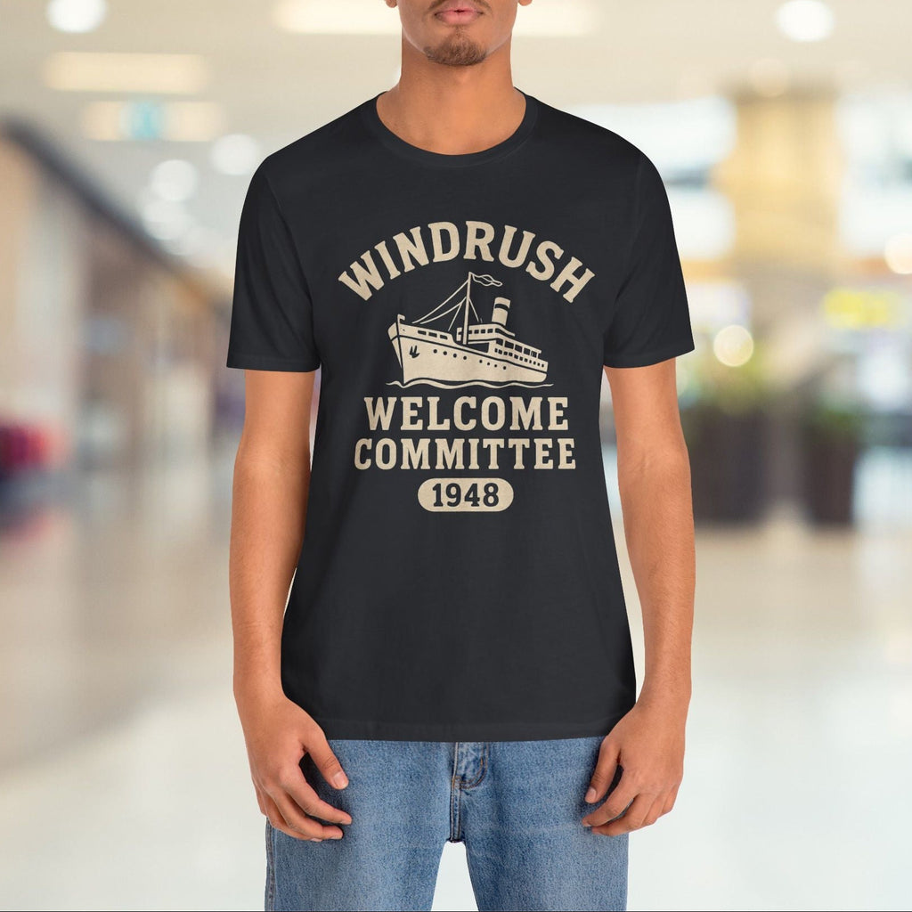 Person wearing a black t-shirt with 'Windrush Welcome Committee 1948' text and graphic in a blurred indoor setting.