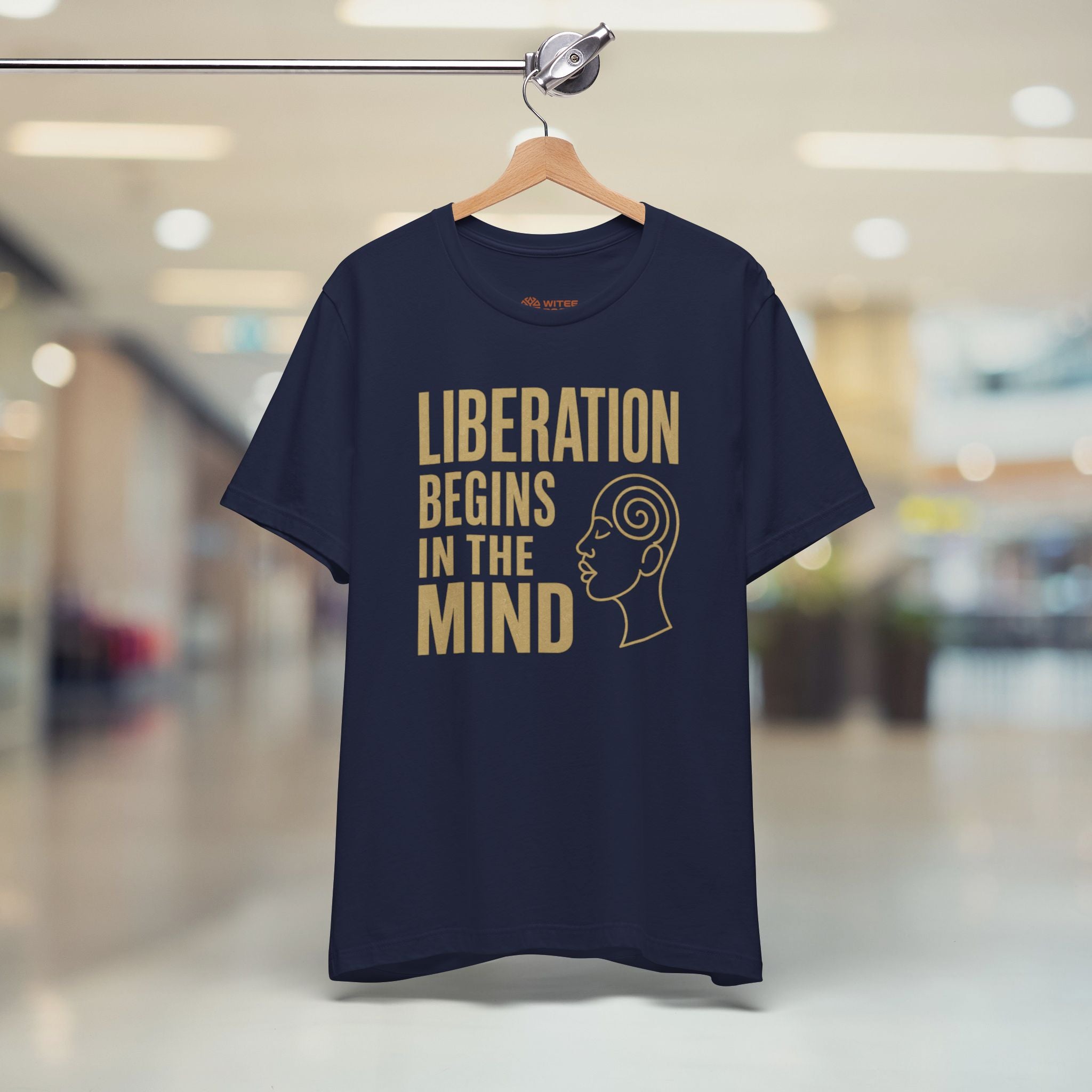 Navy blue t-shirt with 'Liberation Begins in the Mind' text on a hanger in a store.