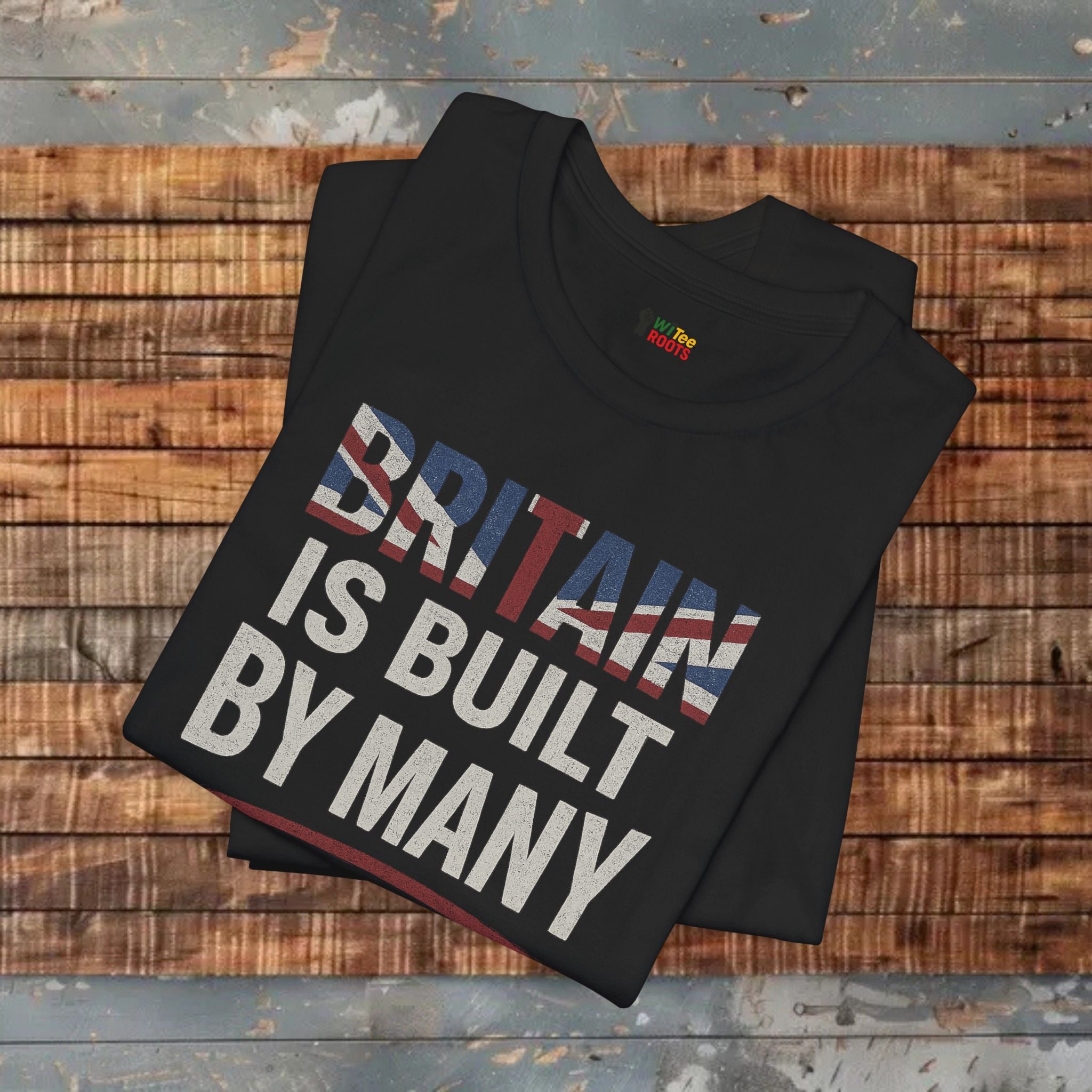 Black t-shirt with 'BRITAIN IS BUILT BY MANY' text on a wooden surface
