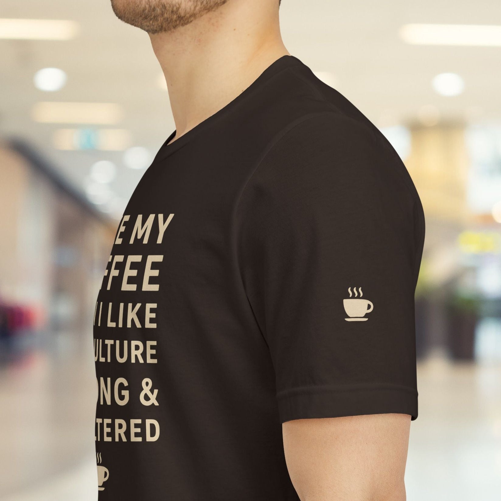 Person wearing a black t-shirt with text and a coffee cup icon in a blurred indoor setting
