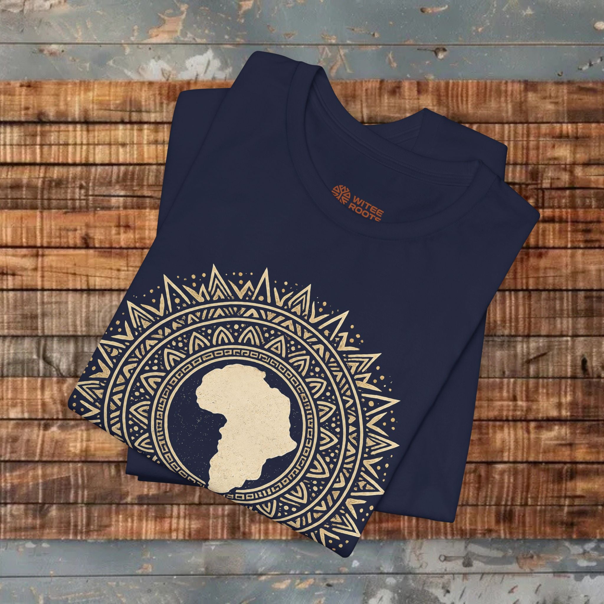 Folded navy blue t-shirt with a gold geometric design and silhouette of Africa on a wooden surface.