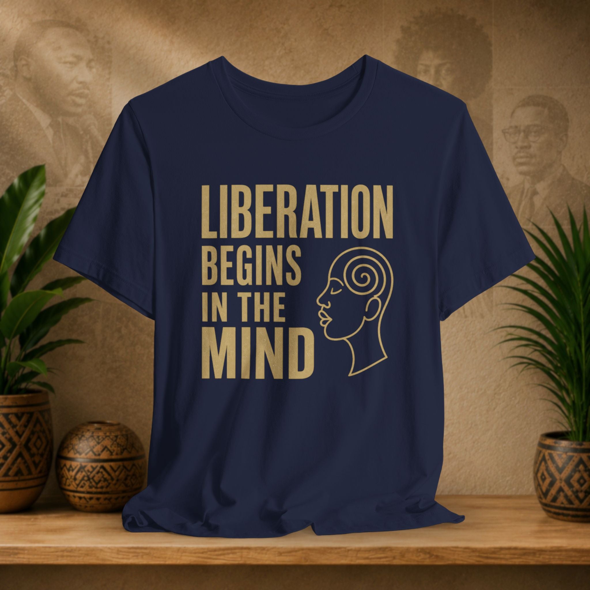 Navy blue t-shirt with 'Liberation Begins in the Mind' text and a profile graphic on a wooden surface with decorative items.