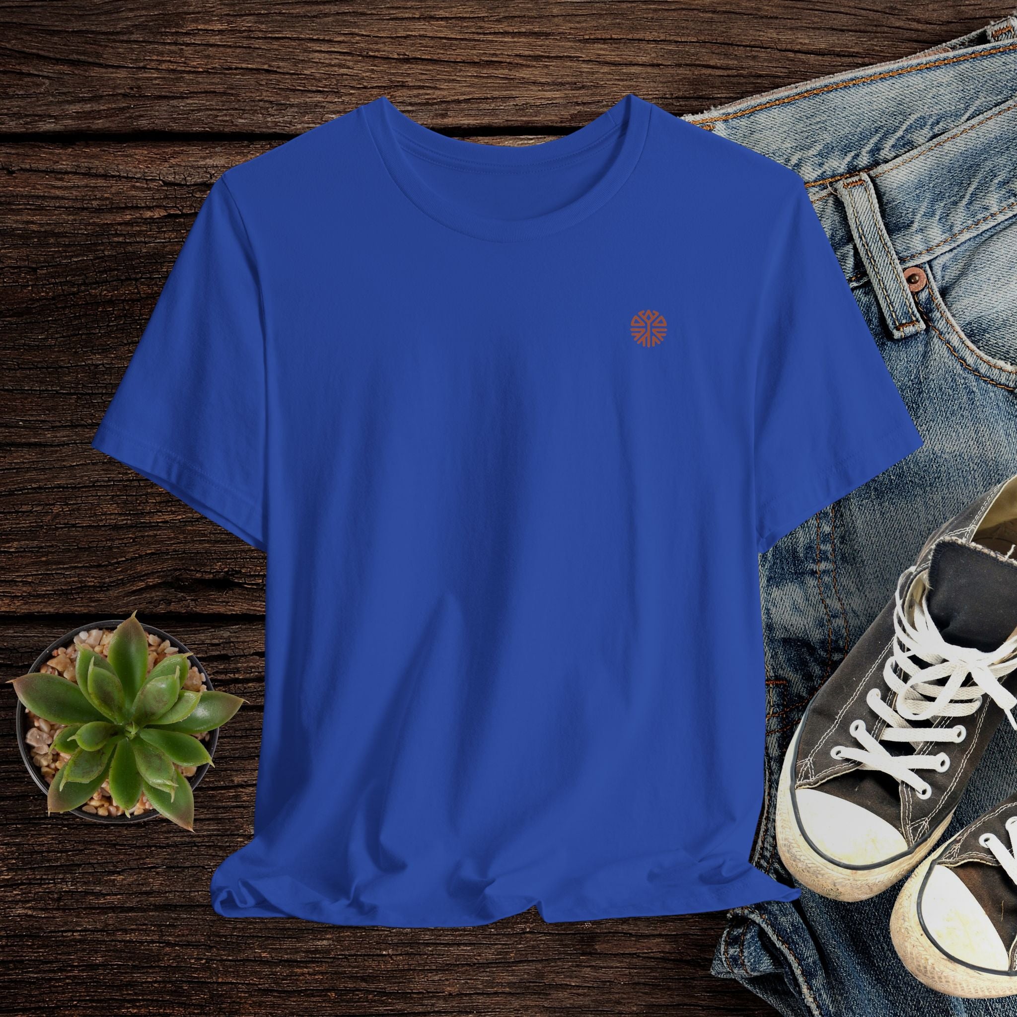 Blue t-shirt with a small logo on a wooden surface with jeans and sneakers.