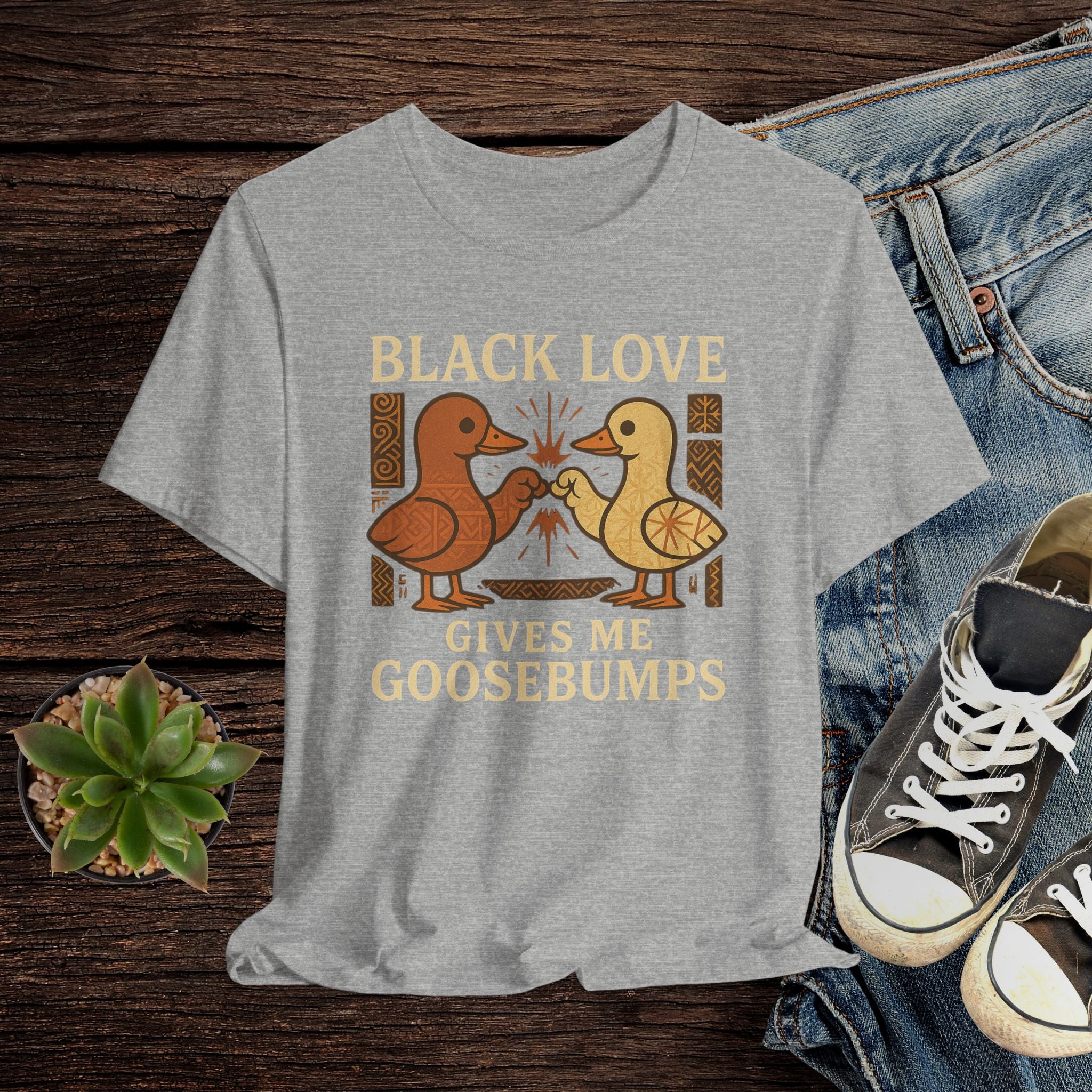Gray t-shirt with 'Black Love Gives Me Goosebumps' graphic on a wooden surface with jeans and sneakers.