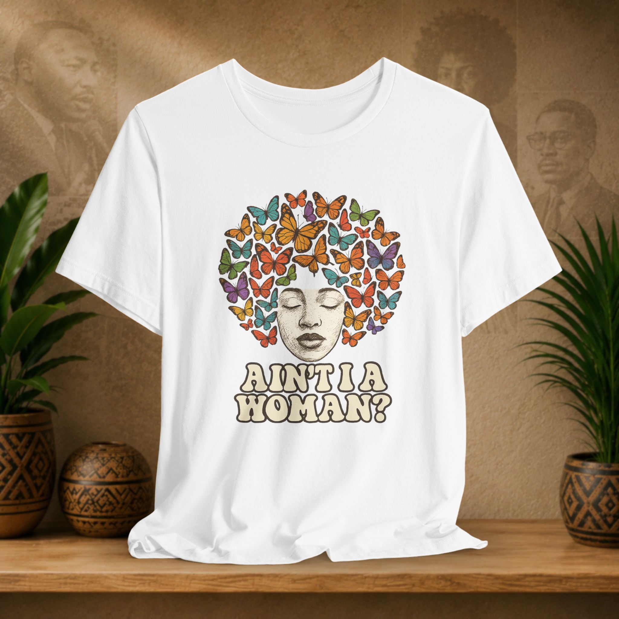 White t-shirt with 'WITEE ROOTS' text on a wooden surface with plants and a textured wall in the background