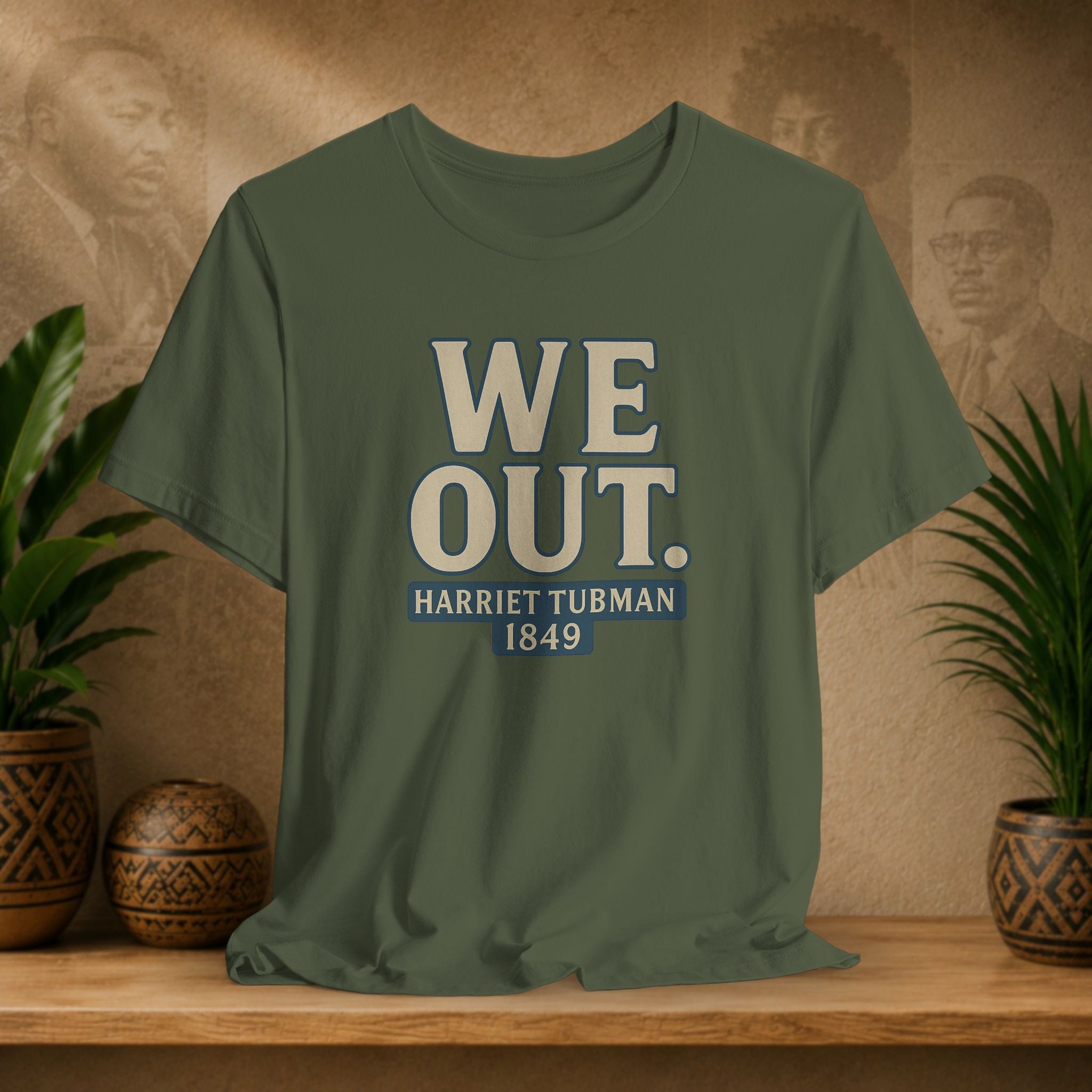 Green t-shirt with 'WE OUT. HARRETT TUBMAN 1849' text on a wooden surface with a decorative background.