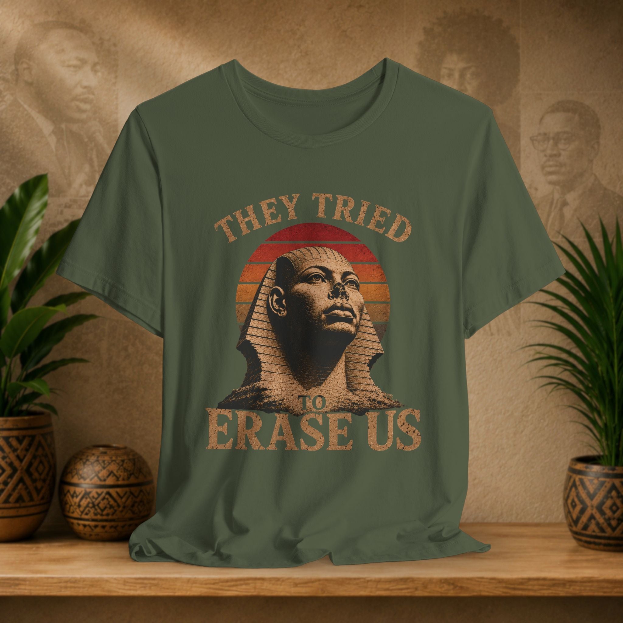 Green t-shirt with Sphinx graphic and text on a wooden surface with plants and wall art in the background