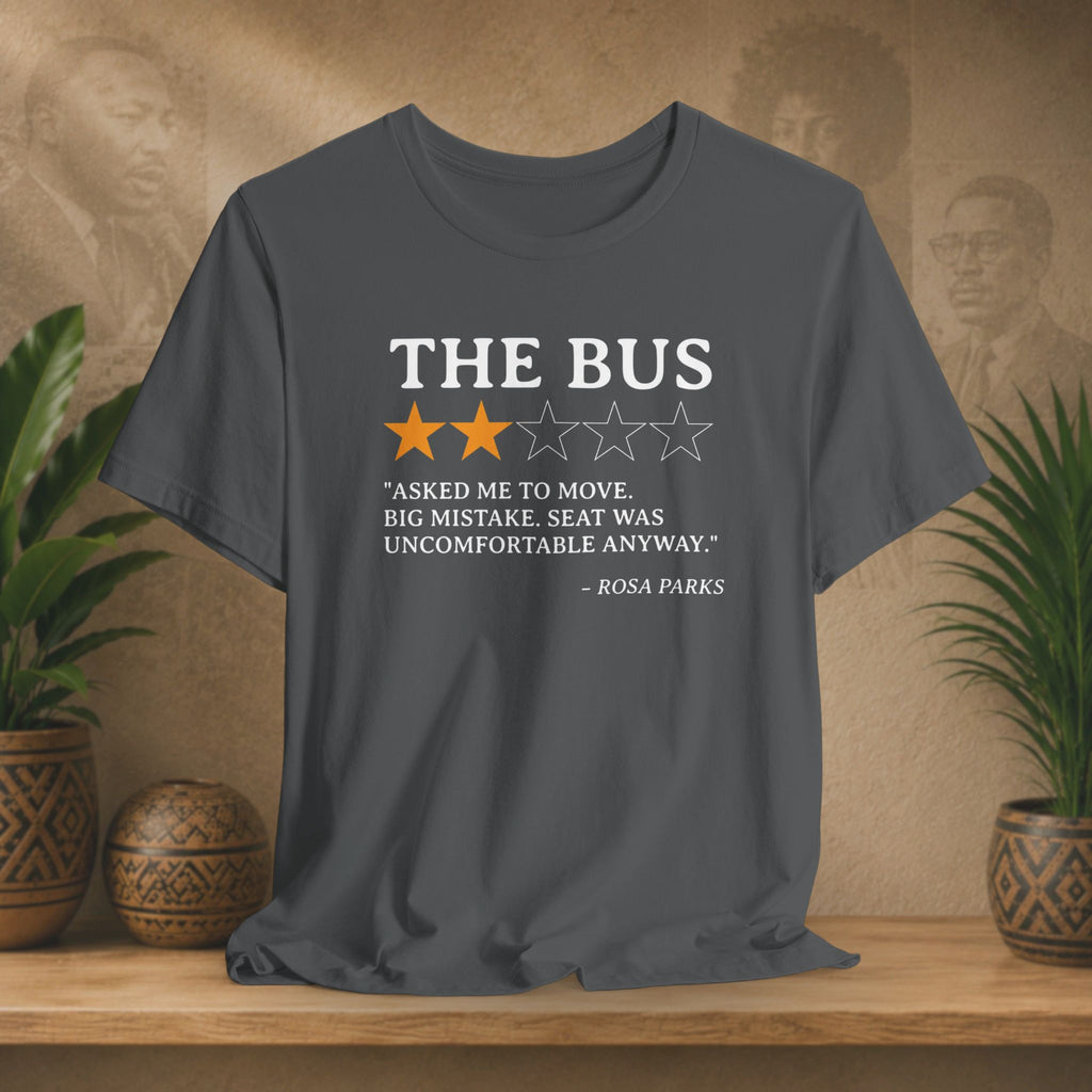 Gray t-shirt with a quote about Rosa Parks on a wooden surface with plants and a patterned wall in the background