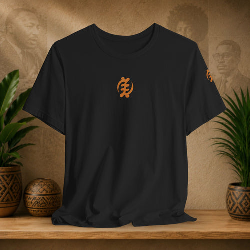 Black t-shirt with orange logo on a wooden surface with plants and wall art in the background