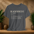 A dark gray graphic t-shirt displayed on a wooden shelf, flanked by potted green plants and decorative ceramic pots against a textured beige background with sepia portraits.
