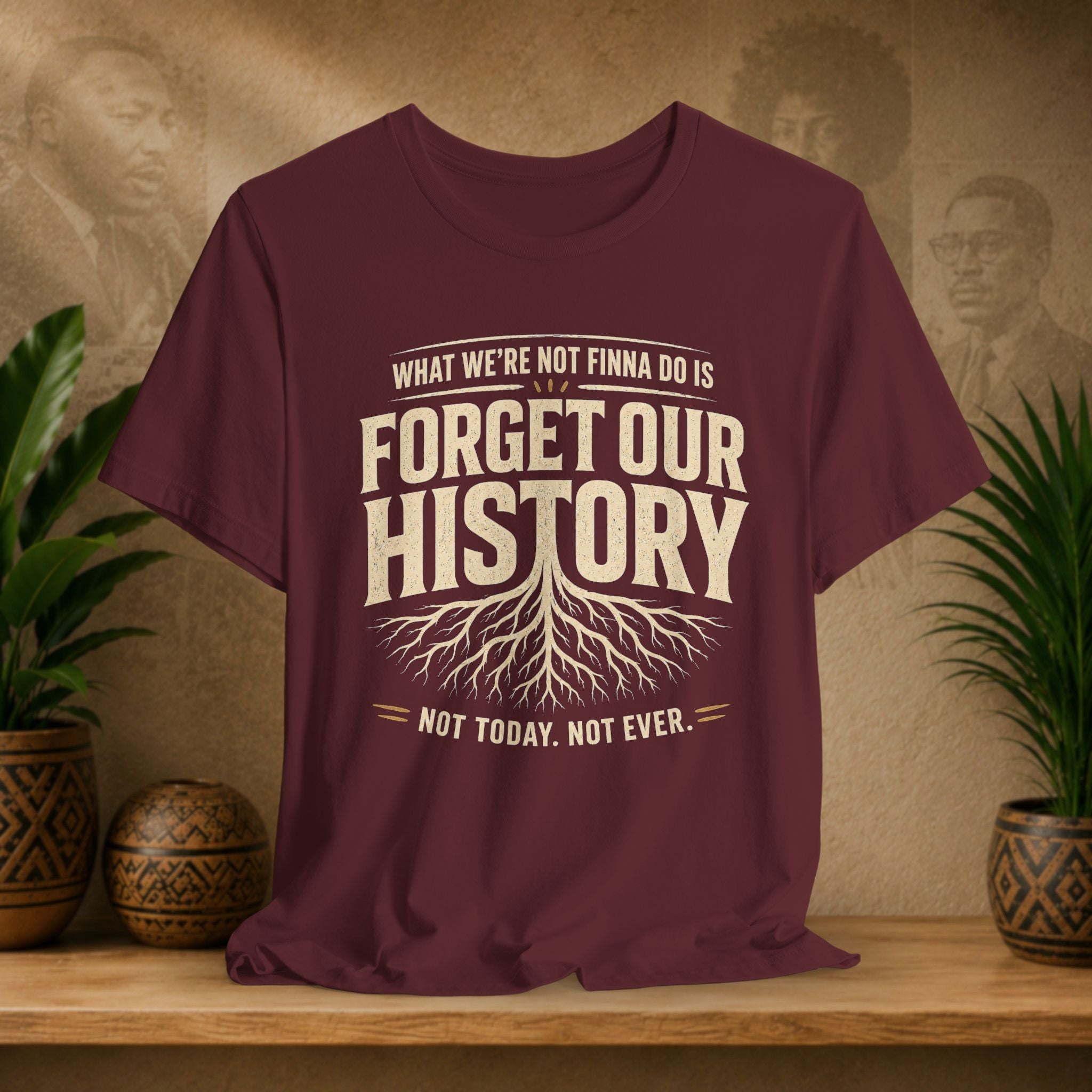 Maroon t-shirt with 'Forget Our History' text on a wooden shelf with plants and a textured wall background