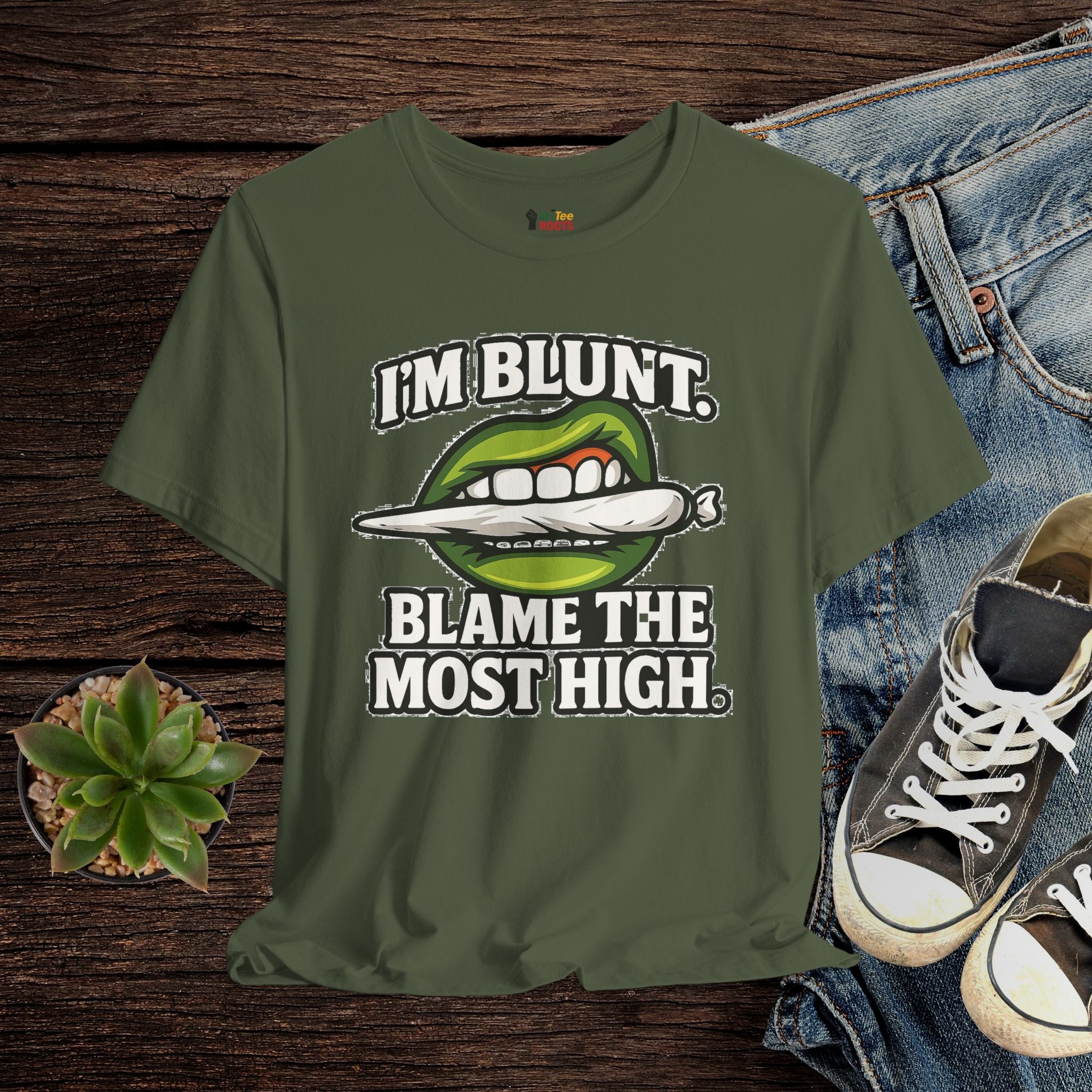 Green t-shirt with graphic design and text on a wooden surface with jeans and sneakers.