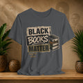 Gray t-shirt with 'Black Books Matter' design on a wooden surface with plants and a textured wall background.