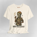 An off-white short-sleeve t-shirt with a graphic of a skeleton wearing a Rasta hat and holding a cigar and a drink, with the text 'BOO-YAKASHA!' printed below. The shirt is shown on a neutral gray background.