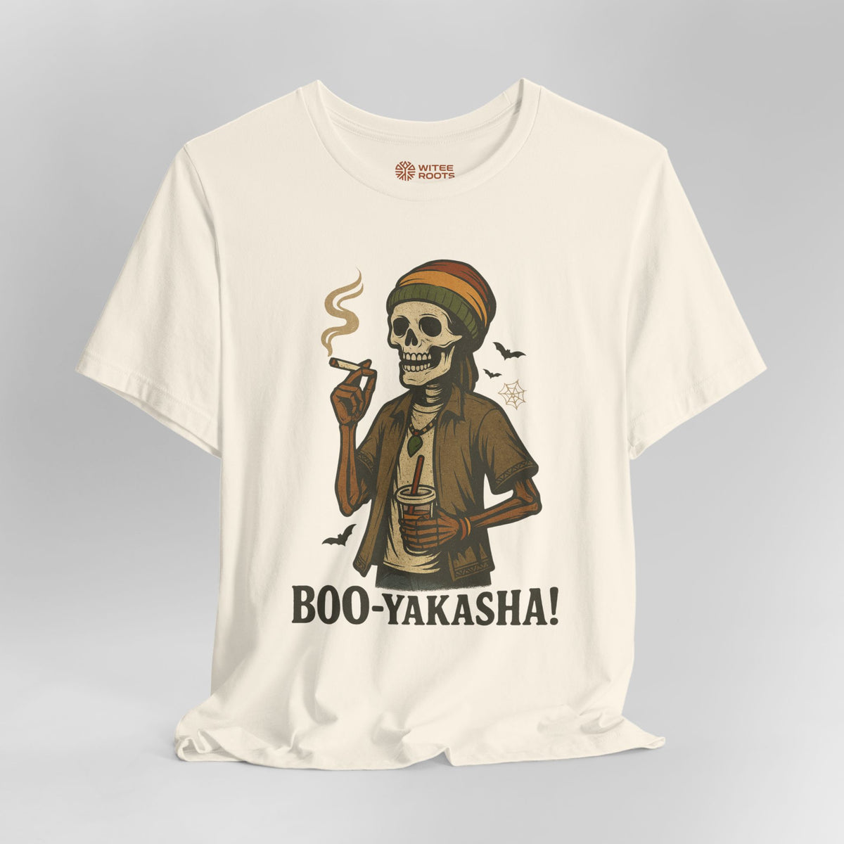 An off-white short-sleeve t-shirt with a graphic of a skeleton wearing a Rasta hat and holding a cigar and a drink, with the text 'BOO-YAKASHA!' printed below. The shirt is shown on a neutral gray background.