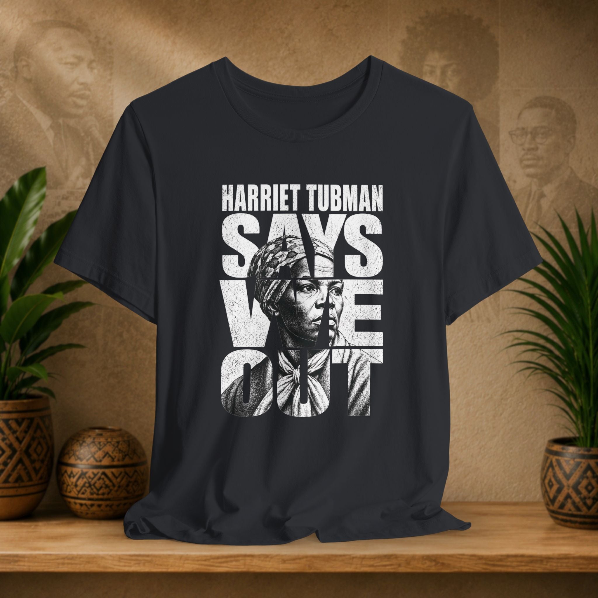 Black t-shirt with Harriet Tubman graphic and text on a wooden surface with plants and decorative items.