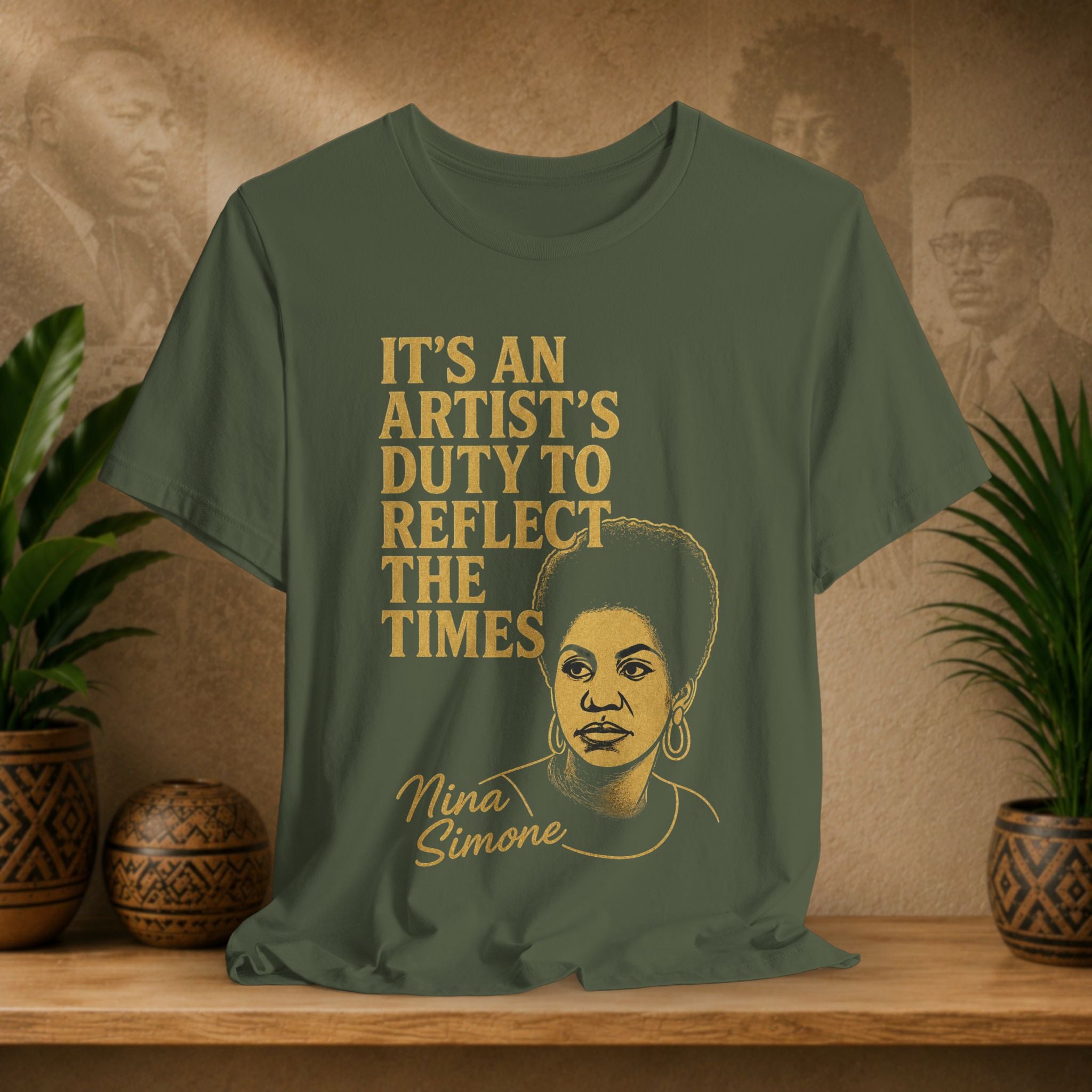Green t-shirt with a graphic of Nina Simone and text on a wooden surface with plants and wall art.