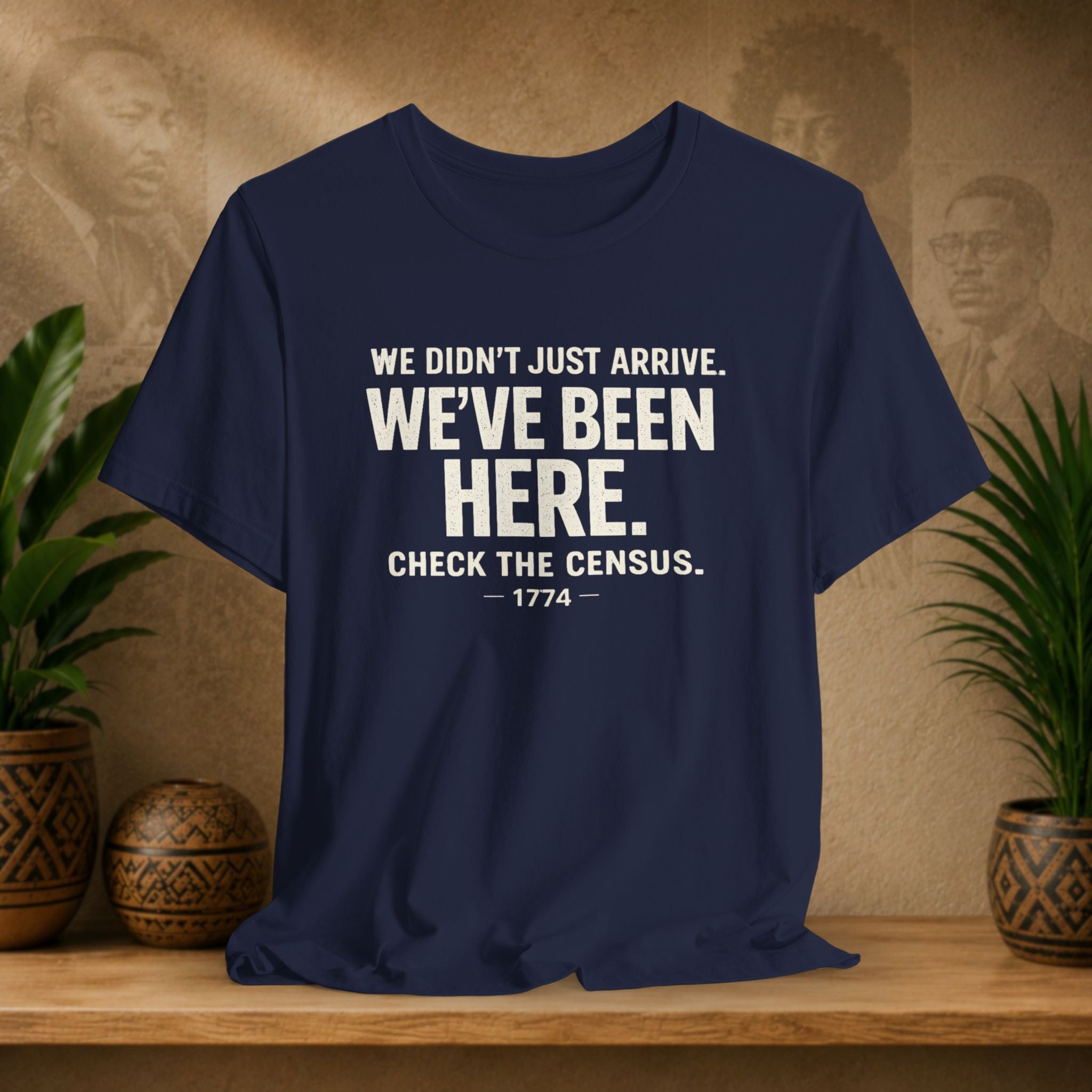 Navy blue t-shirt with white text on a wooden surface with plants and a vintage-style wall in the background