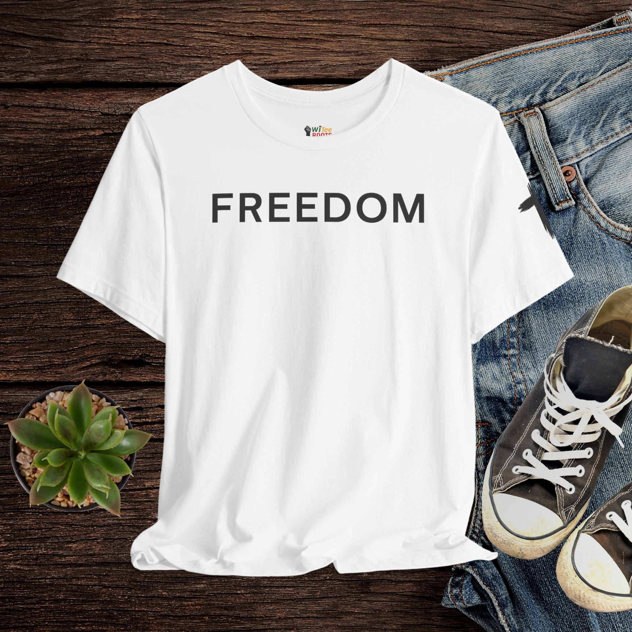 White t-shirt with 'FREEDOM' text on a wooden surface with jeans and sneakers.