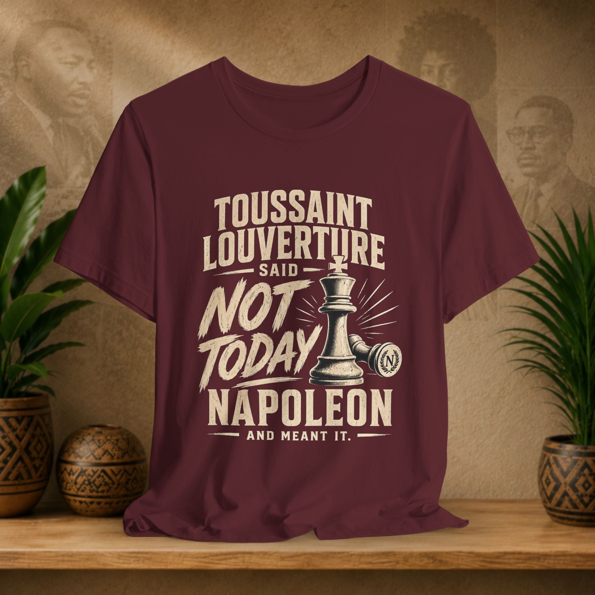 Maroon t-shirt with historical quote design on a wooden surface with plants and portraits in the background