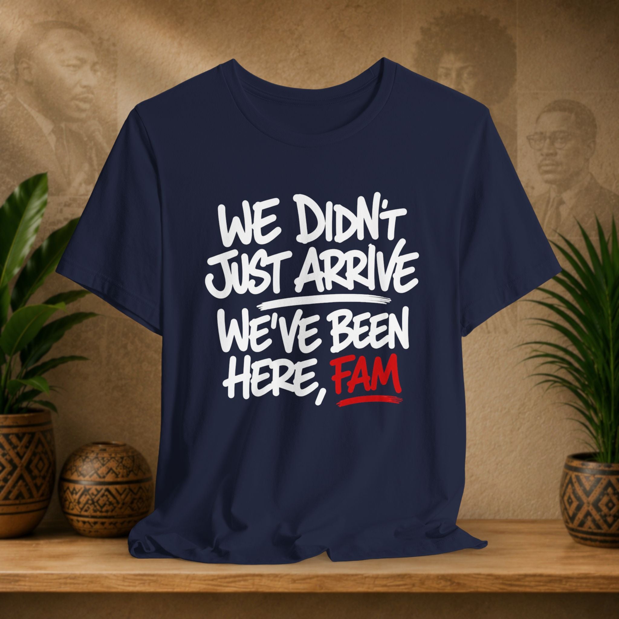Navy blue t-shirt with white and red text on a wooden surface with plants and a textured wall background