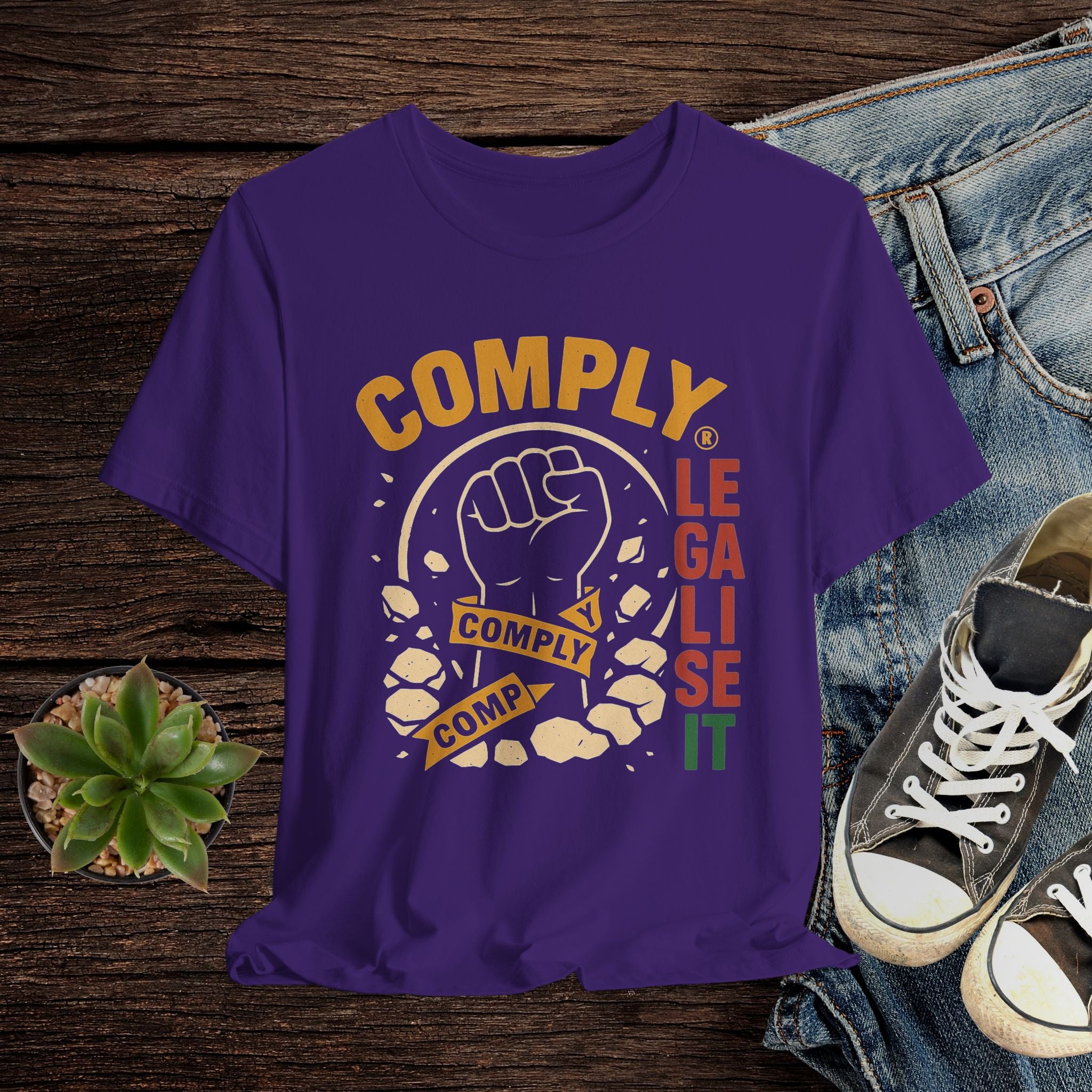 Purple t-shirt with graphic design and text on a wooden surface with jeans and sneakers.