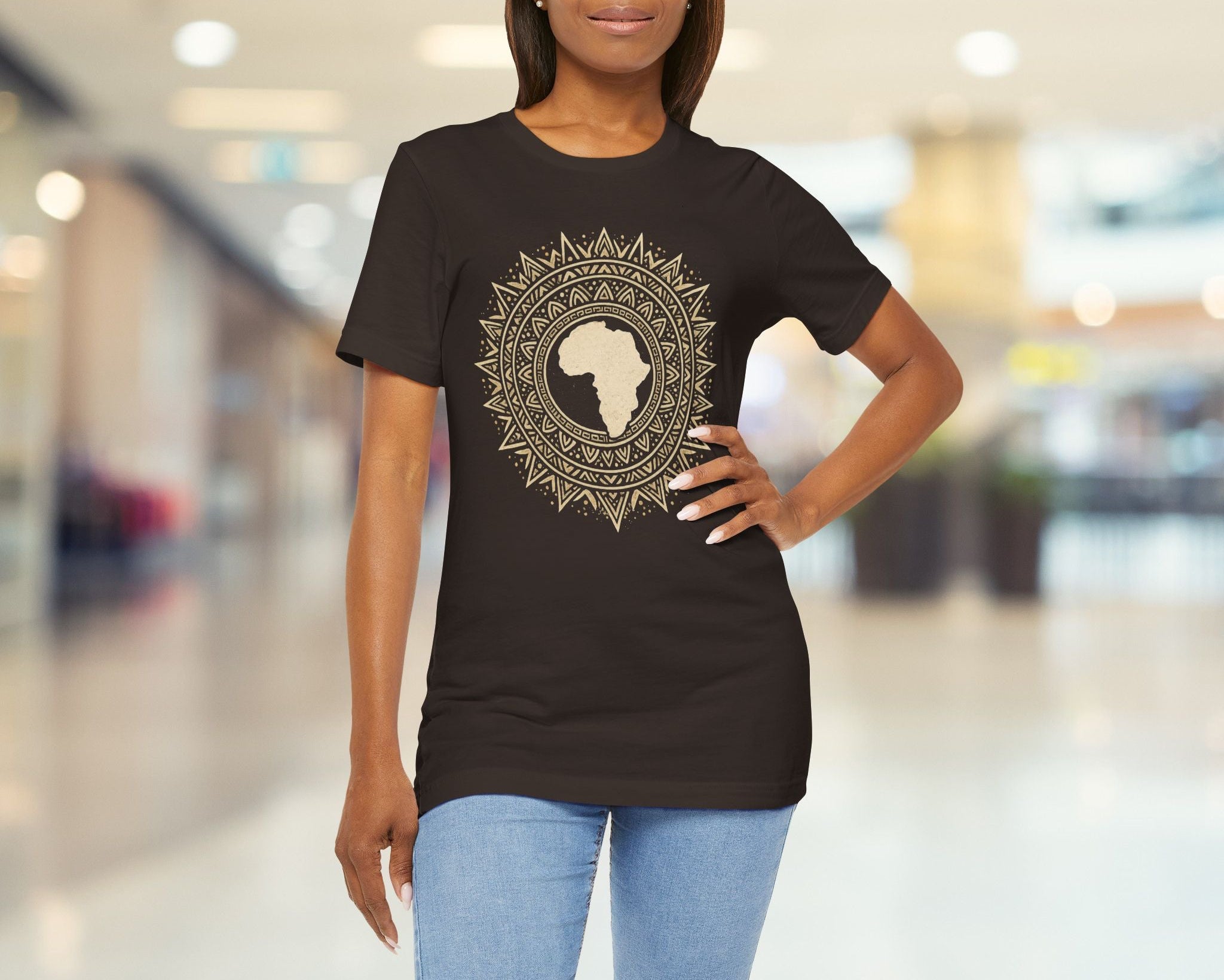 Woman wearing a brown t-shirt with a decorative design in a blurred indoor setting