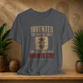 Gray t-shirt with a graphic and text on a wooden surface with plants and decorative items.