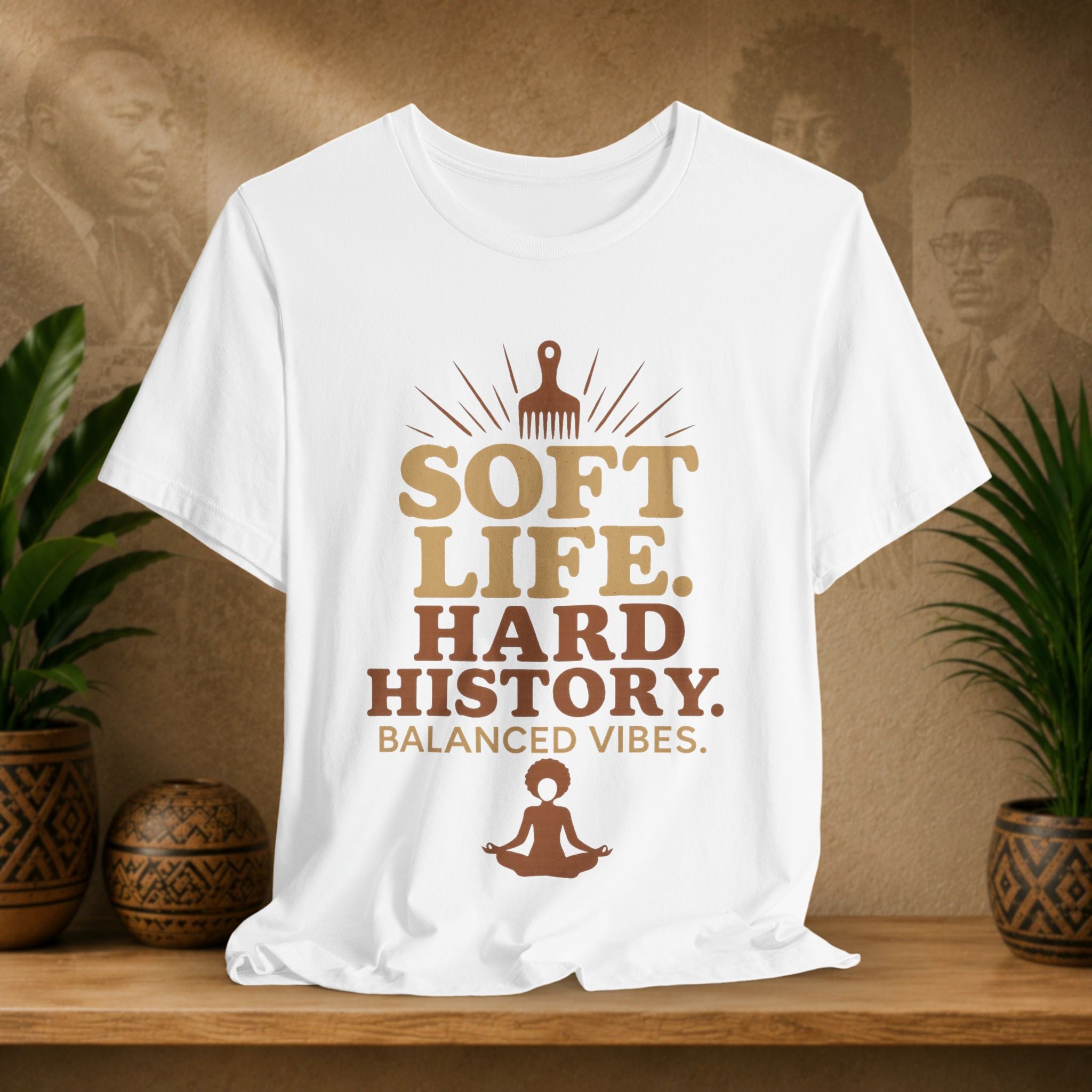 White t-shirt with brown text and graphics on a wooden surface with plants and decorative items.