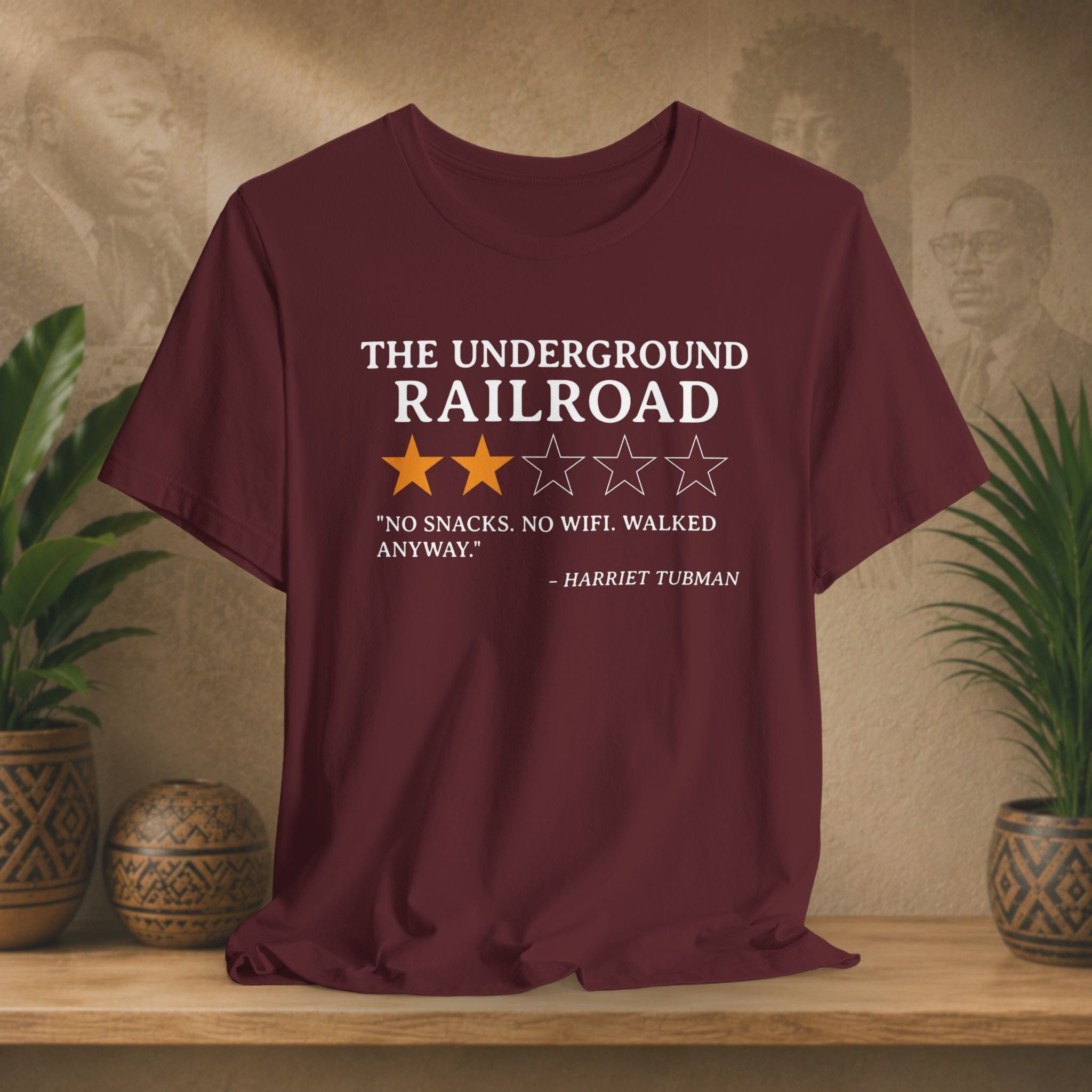 Maroon t-shirt with text and stars on a wooden surface with plants and a textured wall background