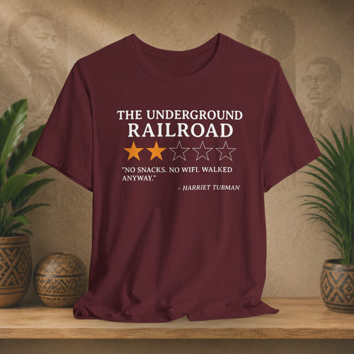 Maroon t-shirt with text and stars on a wooden surface with plants and a textured wall background