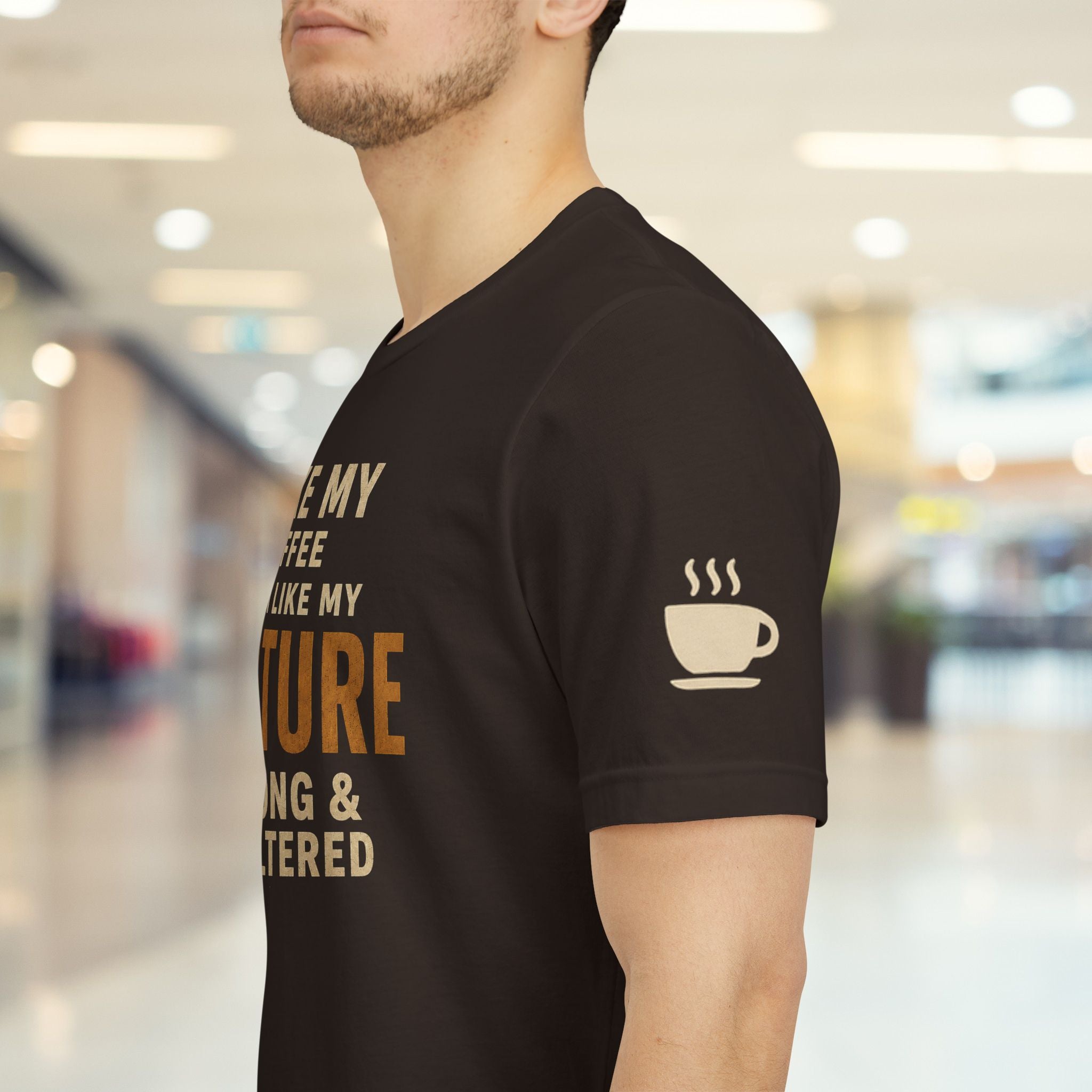 A man wearing a brown t-shirt with a coffee-themed graphic print in beige and brown, standing in a blurred indoor environment.