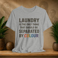 Gray t-shirt with humorous text design on a wooden surface with plants and a textured wall background