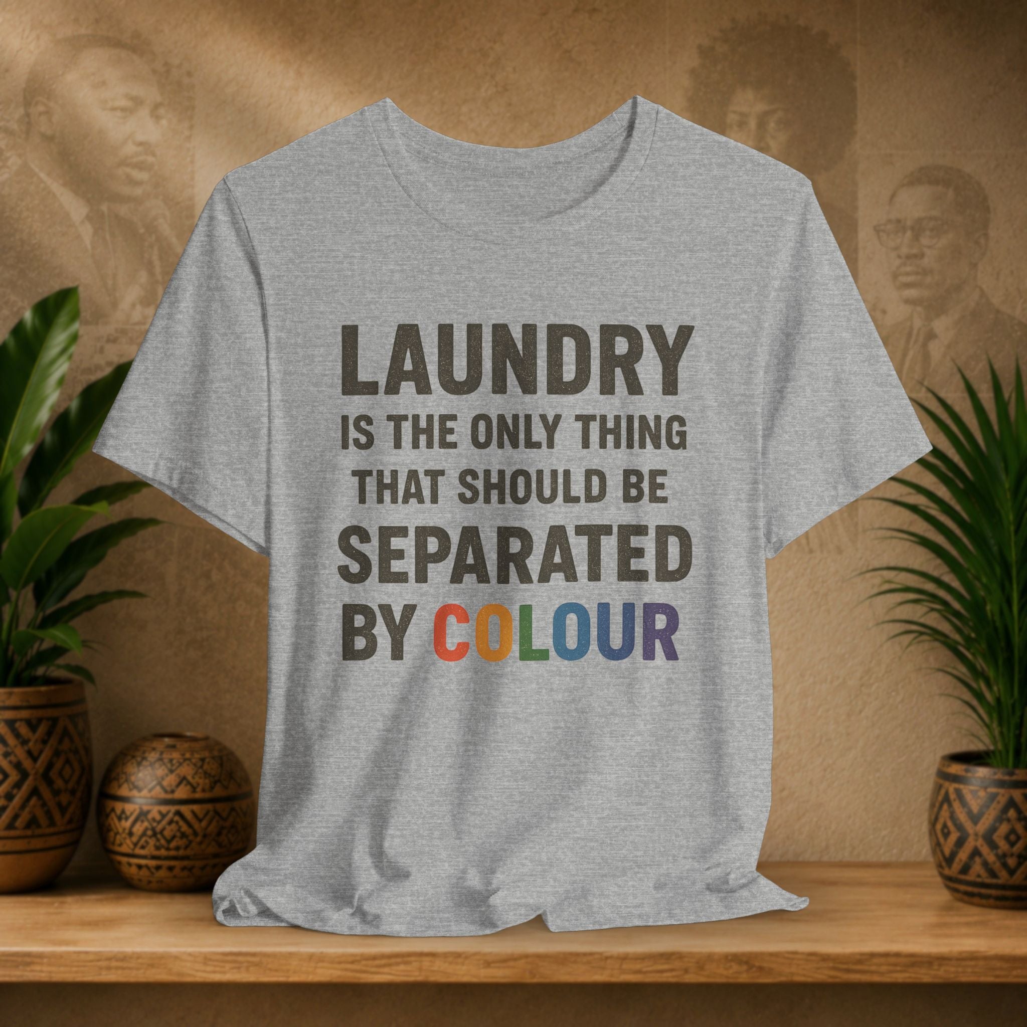 Gray t-shirt with humorous text design on a wooden surface with plants and a textured wall background