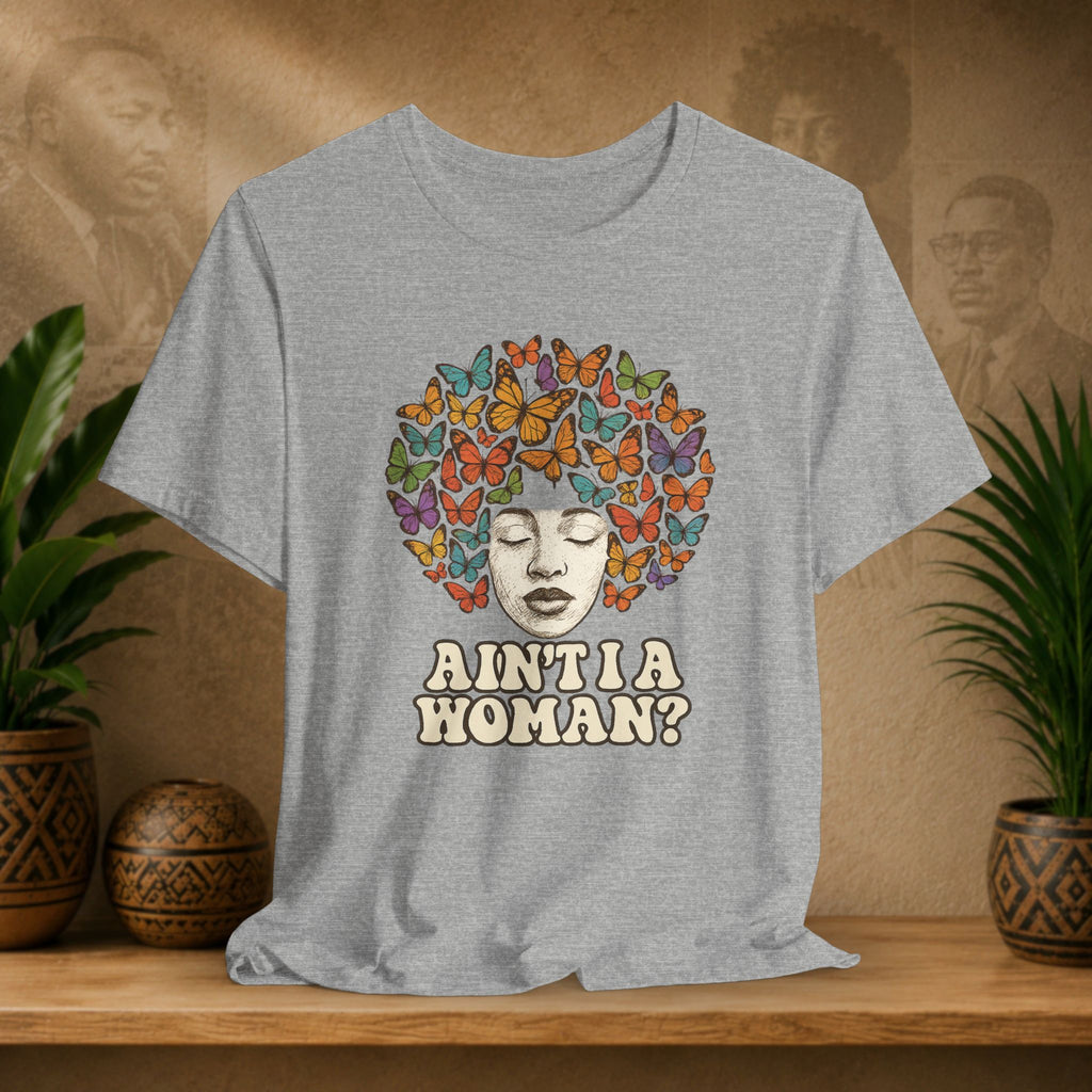 Gray t-shirt with a colorful butterfly design and text on a wooden shelf with plants and decorative items.