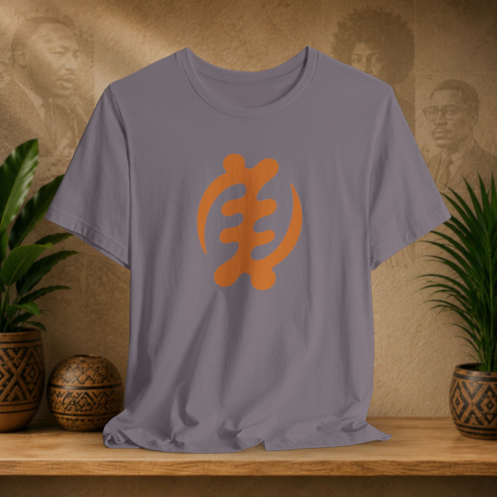 Gray t-shirt with orange symbol on a wooden surface with decorative plants and background.