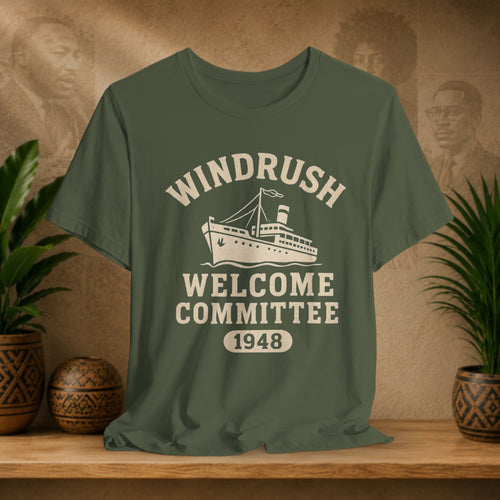 Green t-shirt with 'Windrush Welcome Committee 1948' design on a wooden surface with plants and a decorative wall.