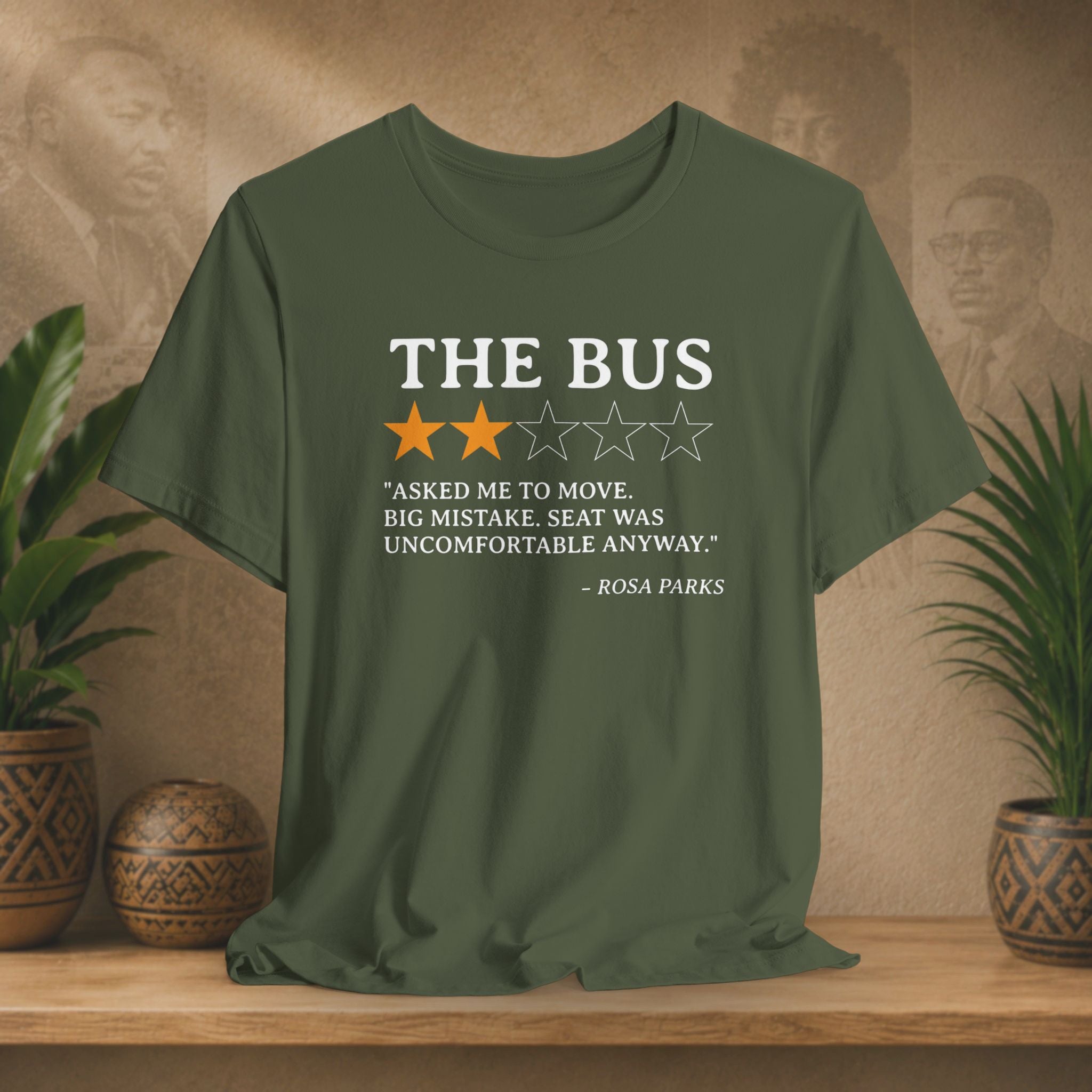 Green t-shirt with a quote on it displayed on a wooden surface with plants and a wall in the background.
