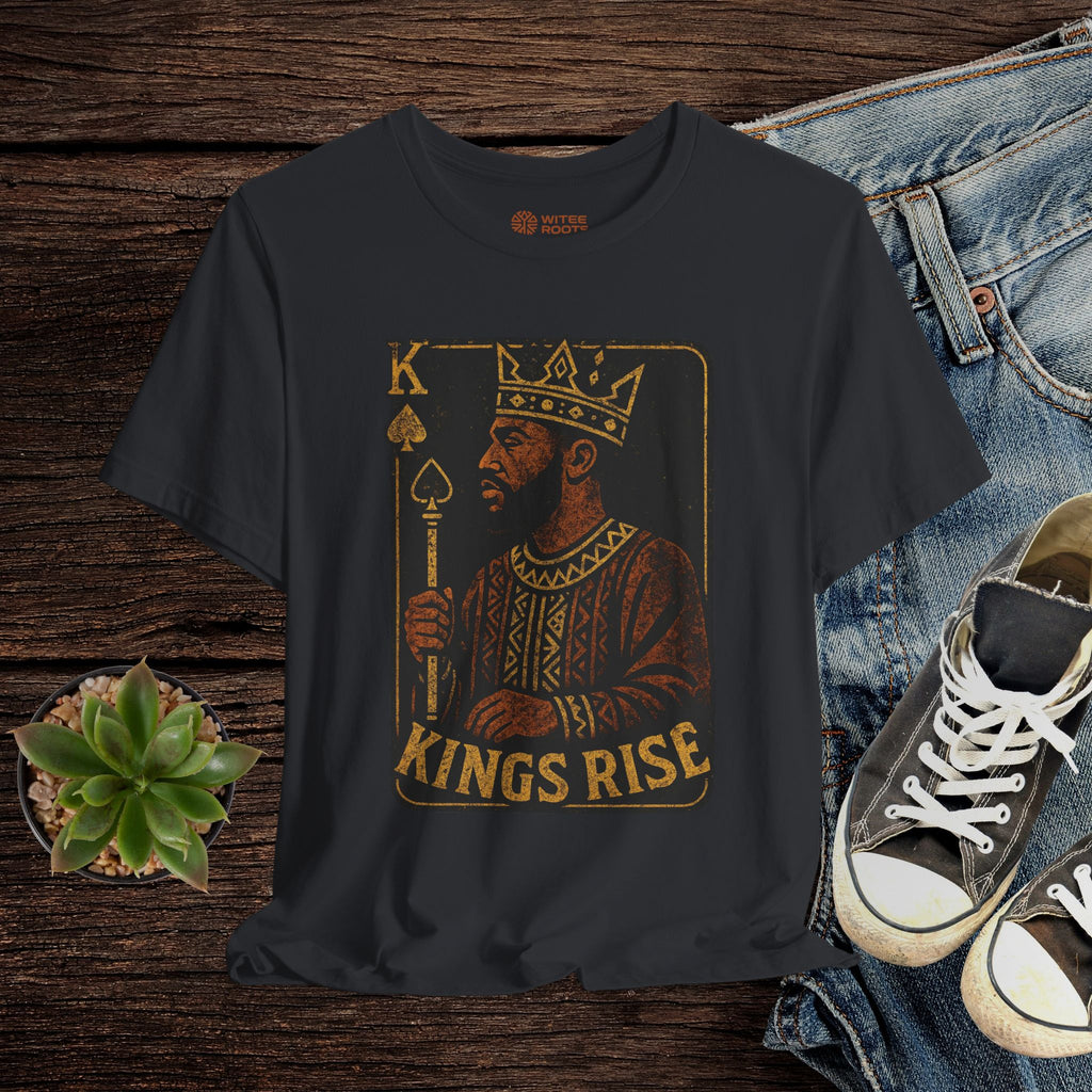 Black t-shirt with 'Kings Rise' graphic design on a wooden surface with jeans and sneakers.
