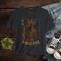 Black t-shirt with 'Kings Rise' graphic design on a wooden surface with jeans and sneakers.